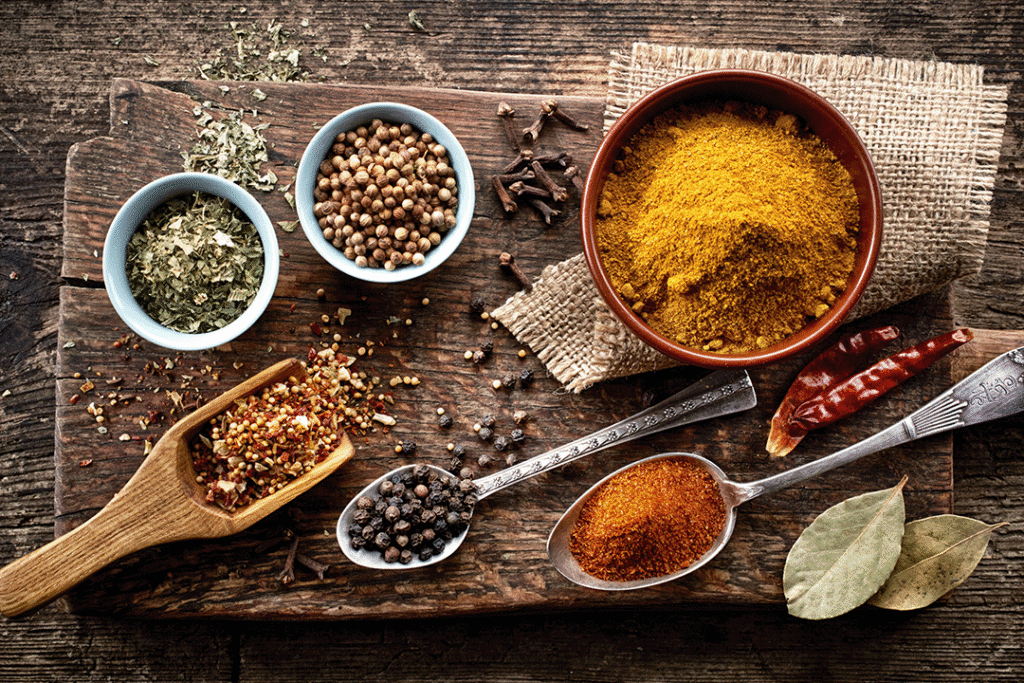 A selection of fresh and ground spices in pots and on spoons on a serving board