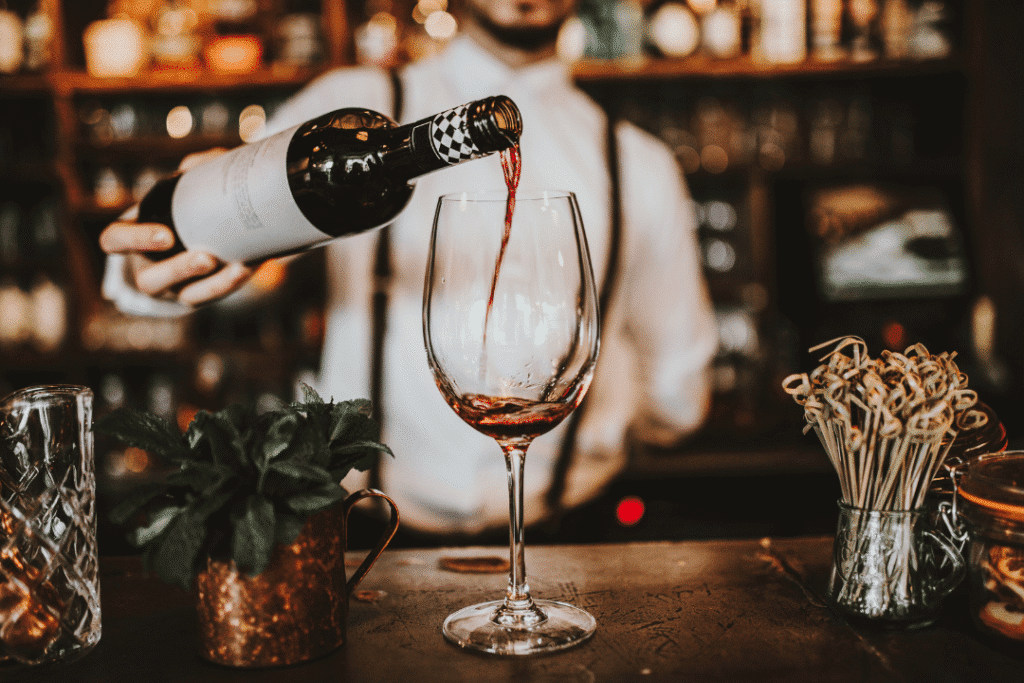 Bartender pouring red wine into glass.